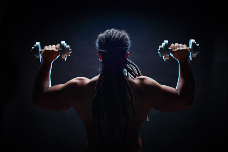 A strong athlete lifts dumbbells in a shoulder press, highlighting strength training, muscle building, and fitness workouts at top gyms in Lubbock.