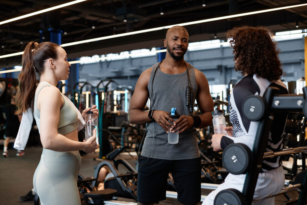 A group of gym-goers chatting with a trainer at a fitness center, highlighting key etiquette tips from this beginner’s guide to the gym. A friendly and supportive gym environment helps newcomers feel confident in their workouts.