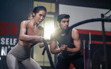 Trainer motivating a woman during battle rope training in a gym while discussing how long should your workouts be.