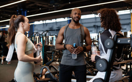 A group of gym-goers chatting with a trainer at a fitness center, highlighting key etiquette tips from this beginner’s guide to the gym. A friendly and supportive gym environment helps newcomers feel confident in their workouts.